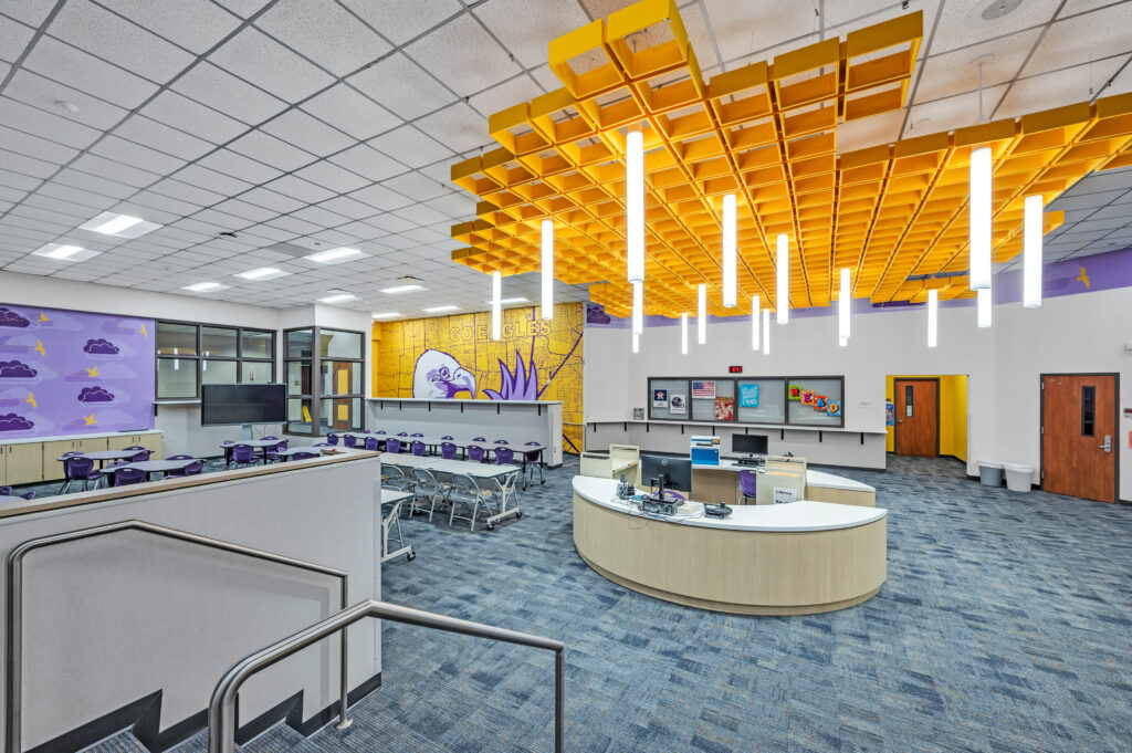 Modern elementary school library and media center in Houston with bold ceiling design, school branding, and classroom seating.